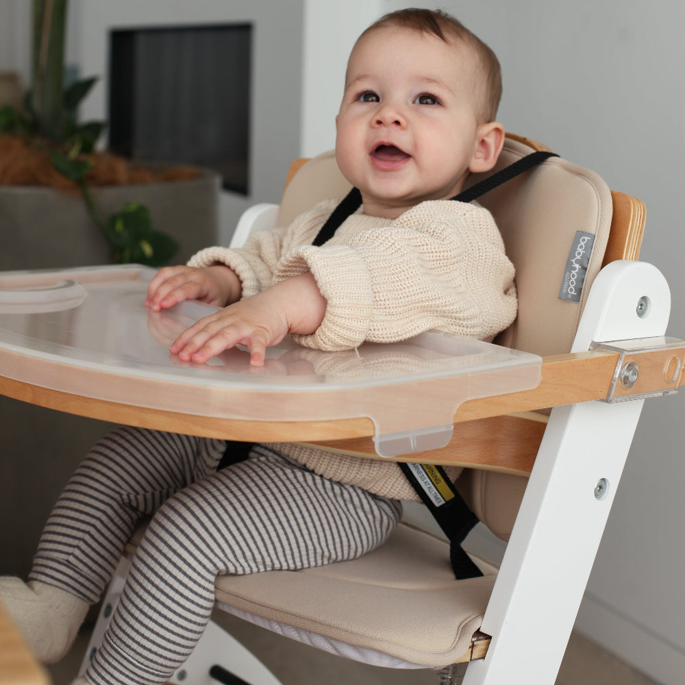 Baby sitting in a high chair with a smiling expression, surrounded by indoor plants.
