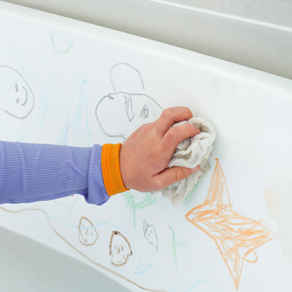 Hand cleaning a bathtub with children's drawings on it
