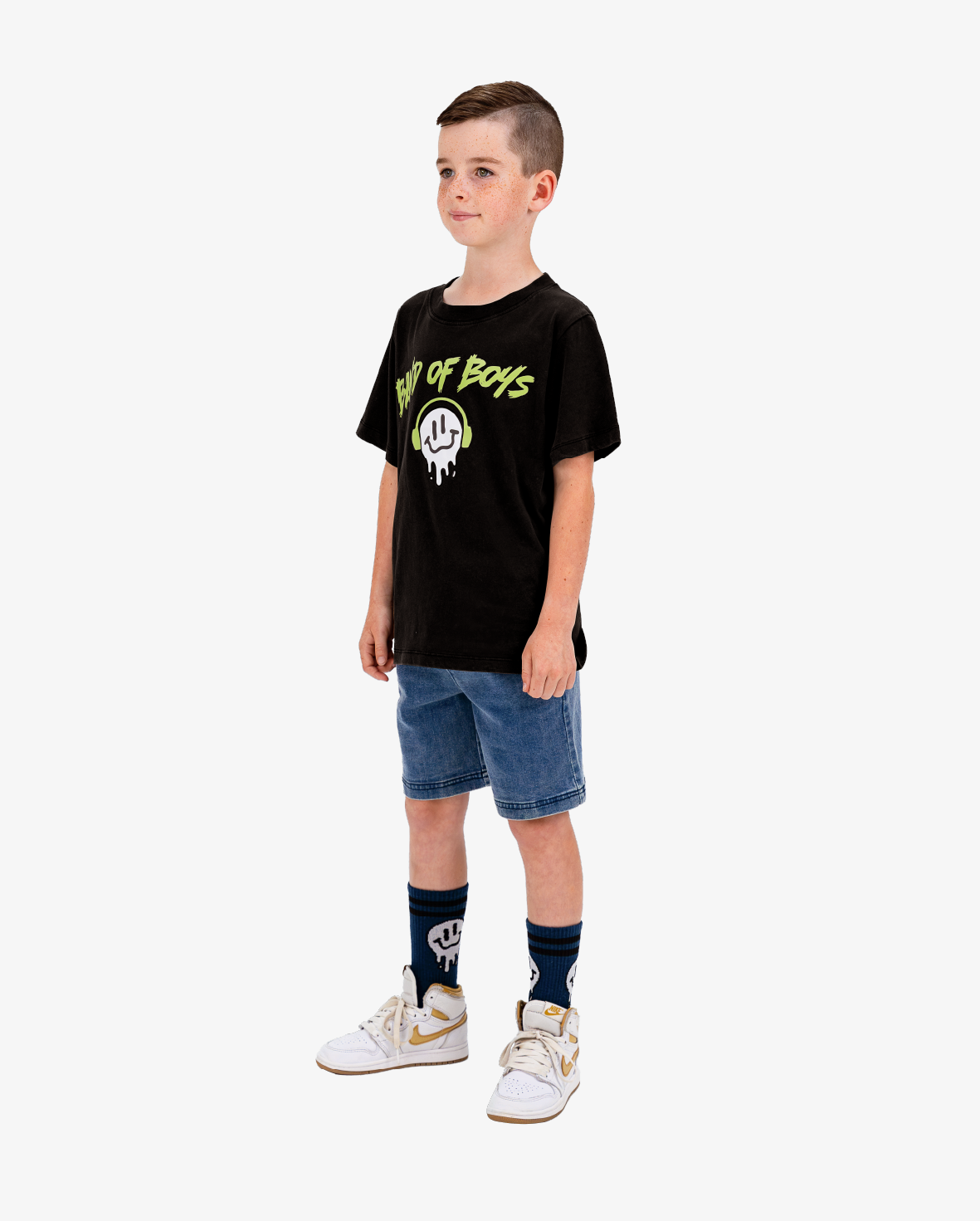 Child wearing a black t-shirt with yellow text and graphics, denim shorts, and white sneakers on a white background