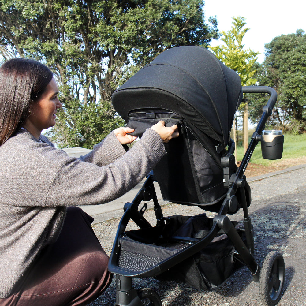 Woman adjusting a black stroller on a road with trees in the background