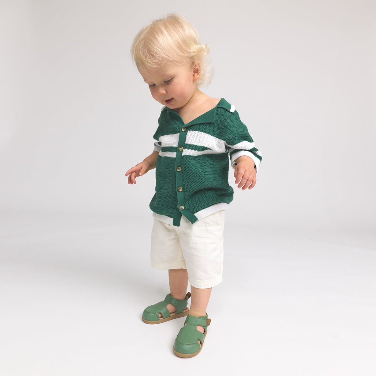 Child wearing a green outfit with white accents on a plain background