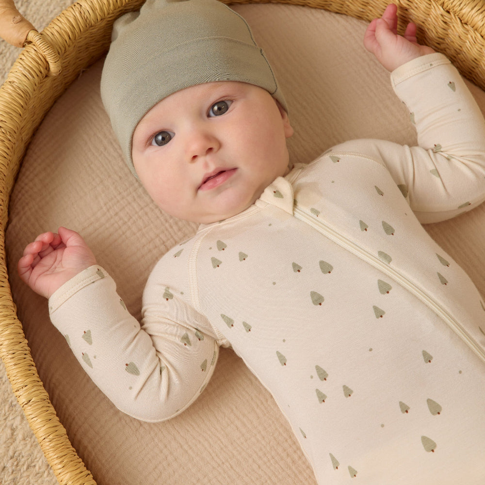 Baby lying in a wicker basket wearing a light-colored outfit with heart patterns and a matching hat.