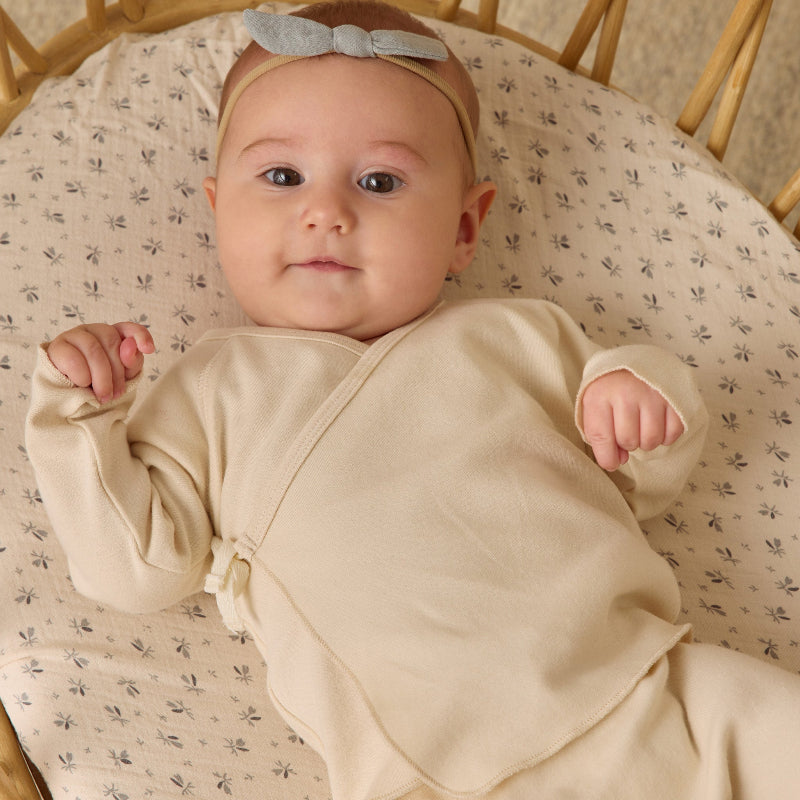 Baby in a beige outfit lying on a floral-patterned blanket