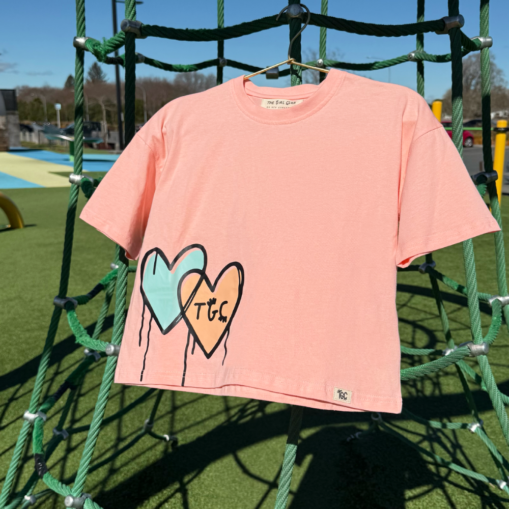 Pink t-shirt with heart designs and 'TLC' text on a playground background