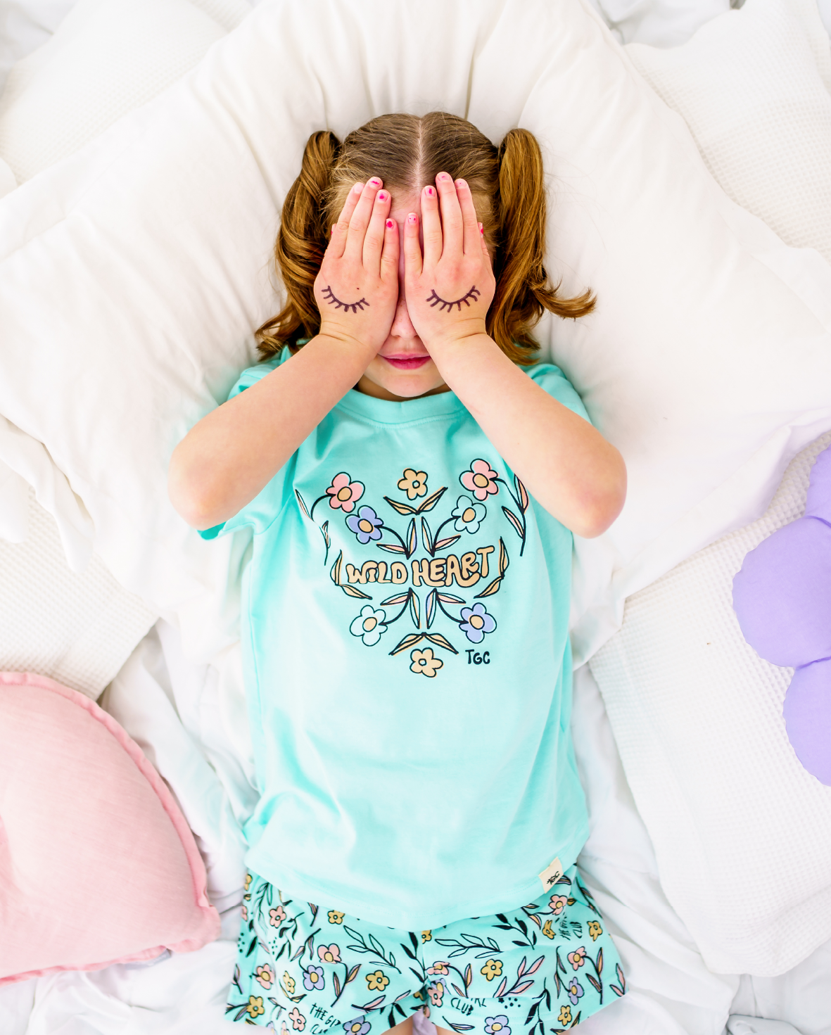 Child wearing a light blue pajama set with floral design and text, lying on a white bed.