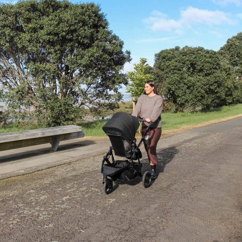 Woman pushing a stroller along a path with trees and a bench in the background