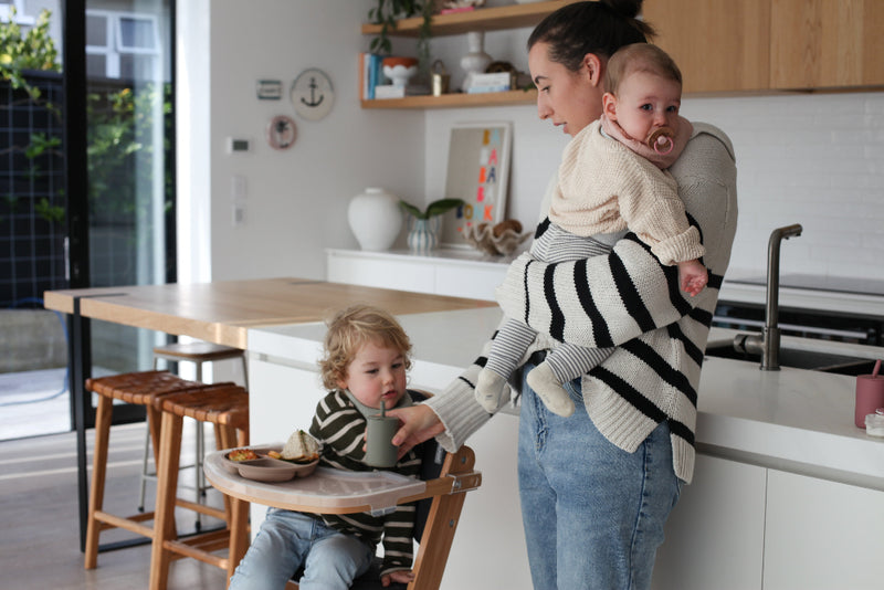 Woman holding a baby and a child sitting at a kitchen table.