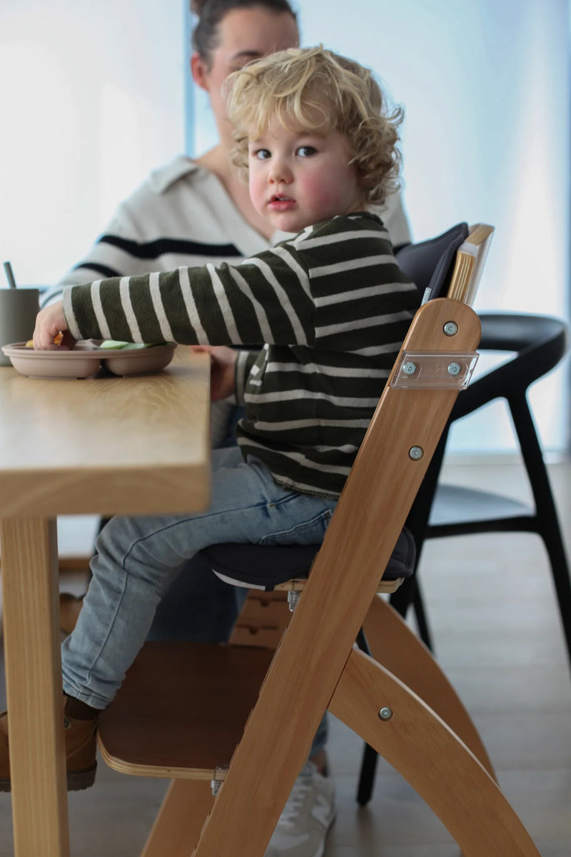 Child sitting in a wooden high chair at a table with a blurred background