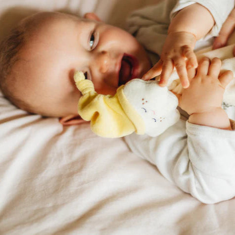 Baby lying on a white blanket with a yellow and white ruffled toy