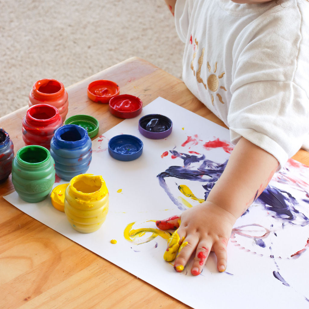 Child painting with colorful paint containers on a wooden table