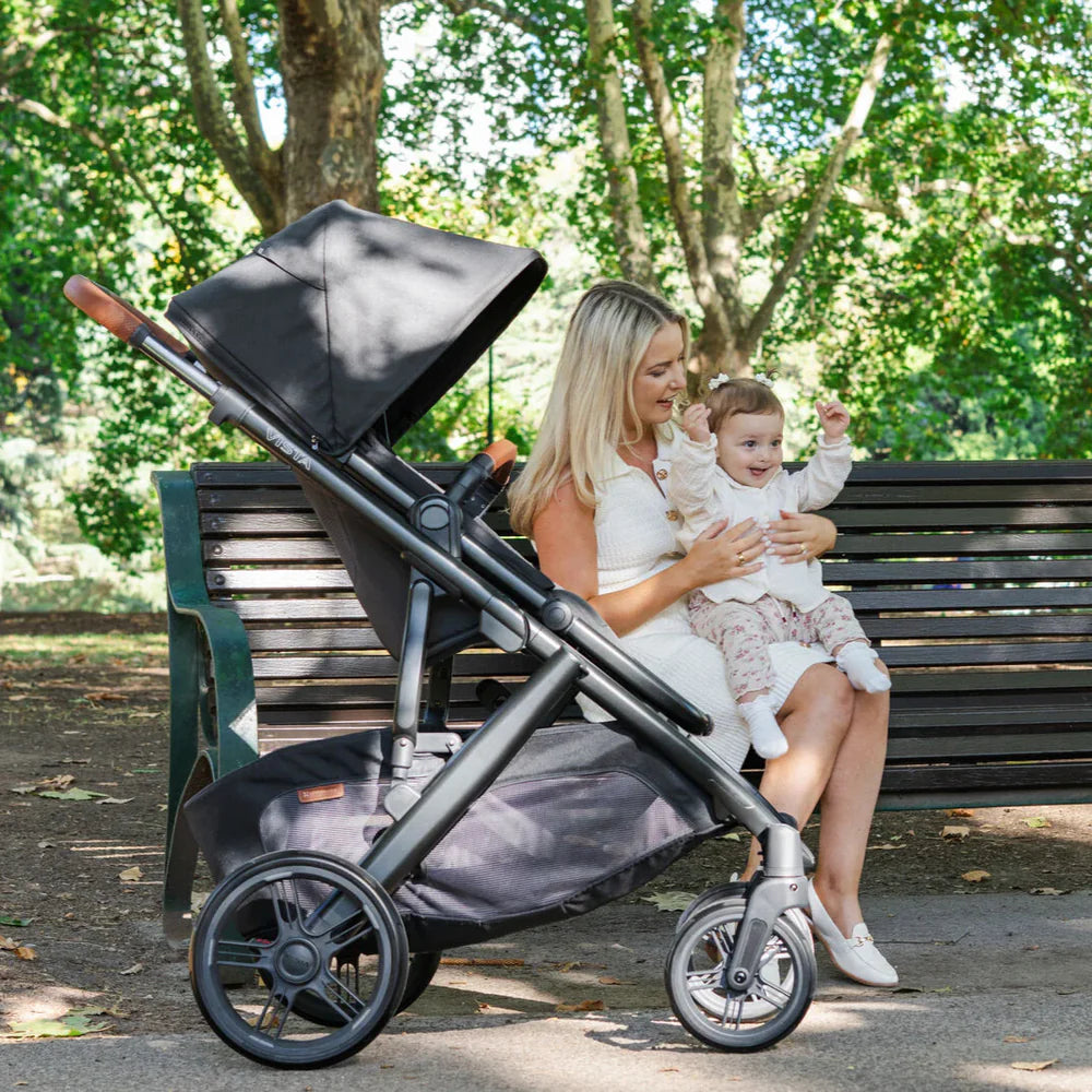 Woman holding a baby and sitting on a bench with a stroller in a park setting