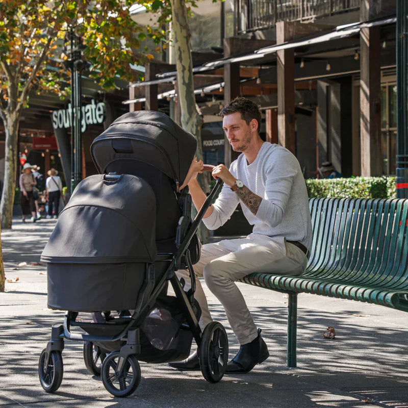 Man sitting on a bench with a stroller in an urban setting